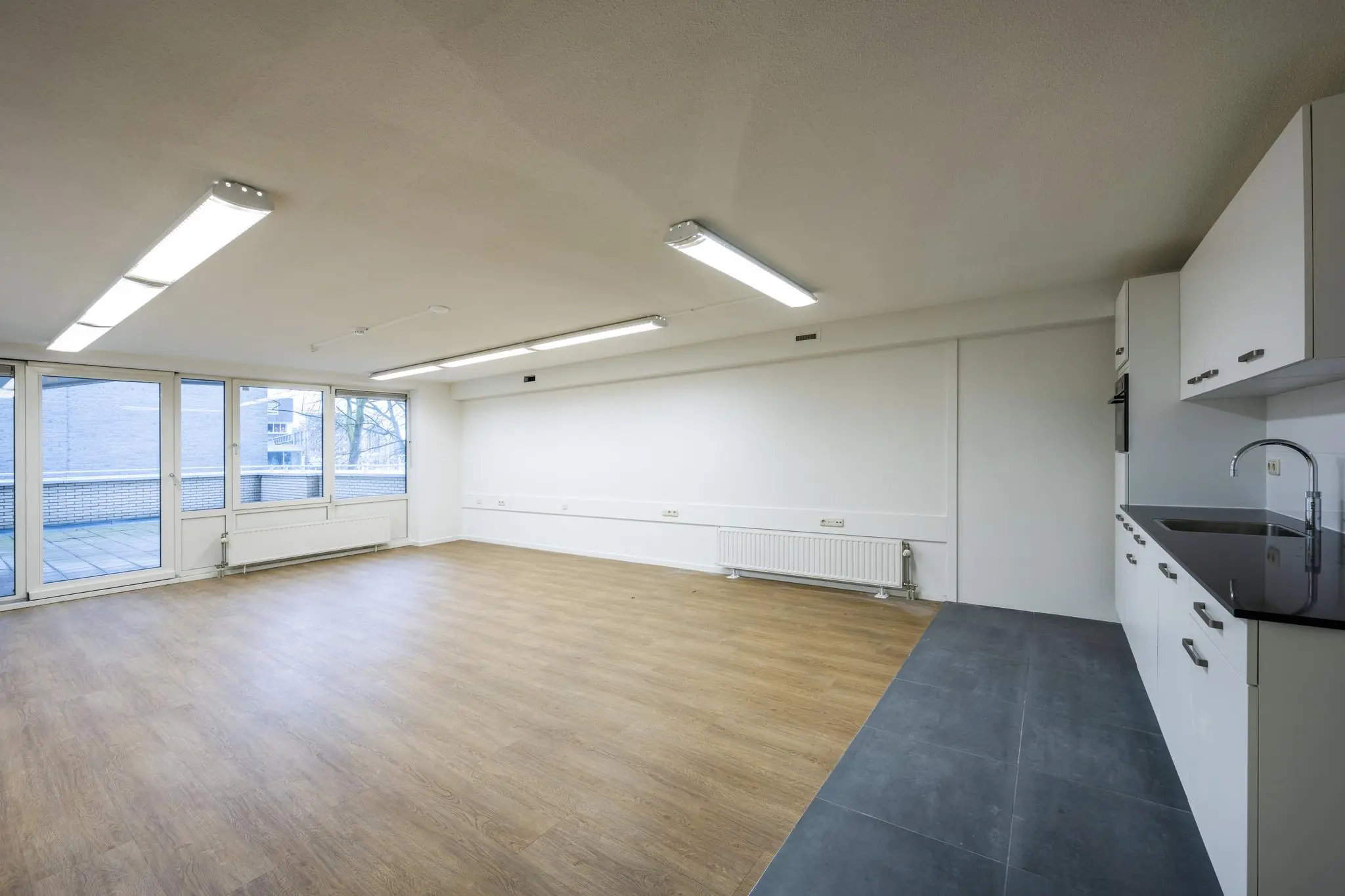 Lichte, lege ruimte met laminaatvloer, moderne kitchenette en grote ramen aan de Prins Hendrikkade.